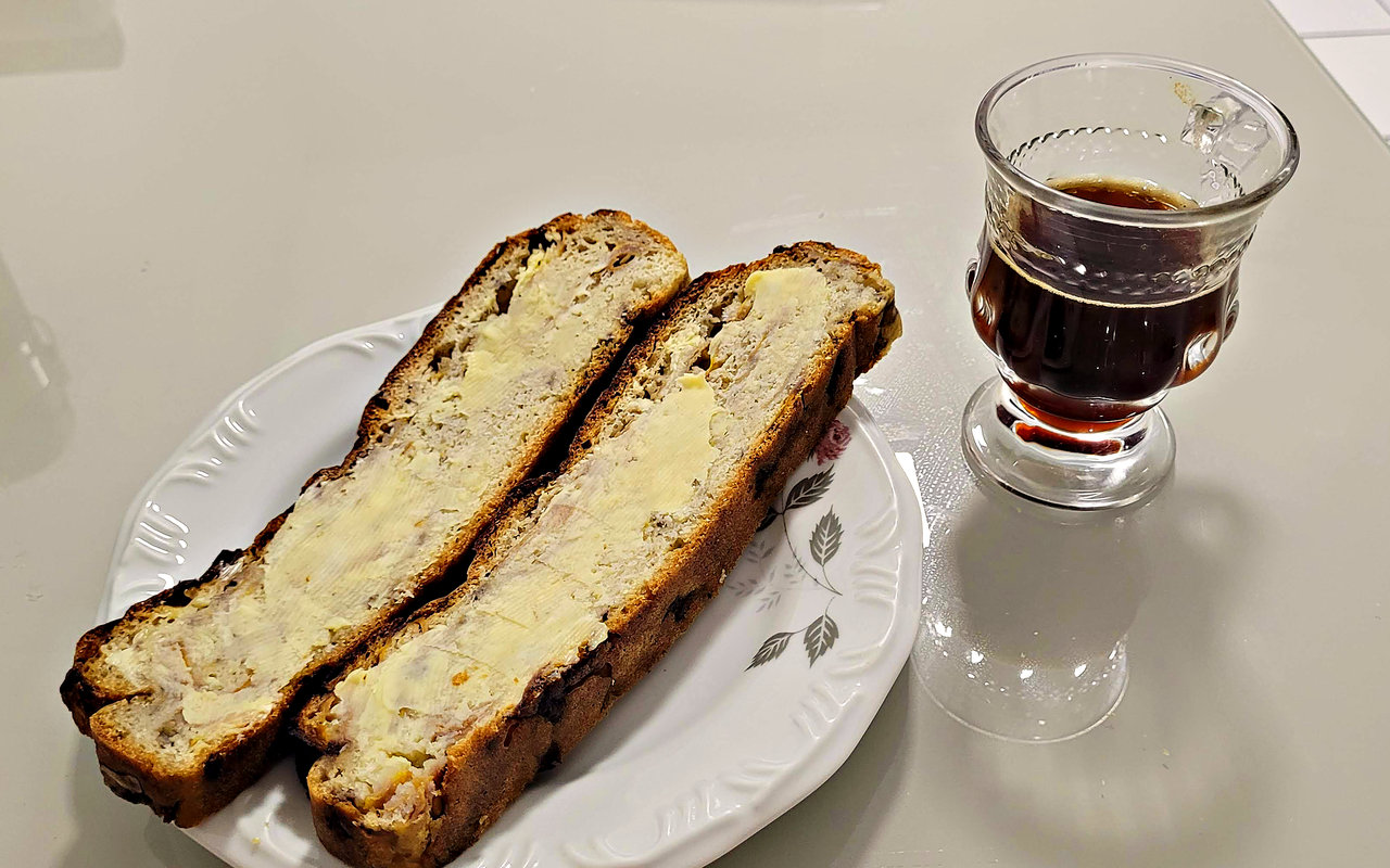 Duas fatias de brote com manteiga num prato, ao lado de um copo de café
